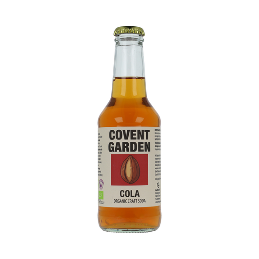 Glass of Covent Garden Cola bio 250ml bottle with dark cola beverage and label, in a natural setting.